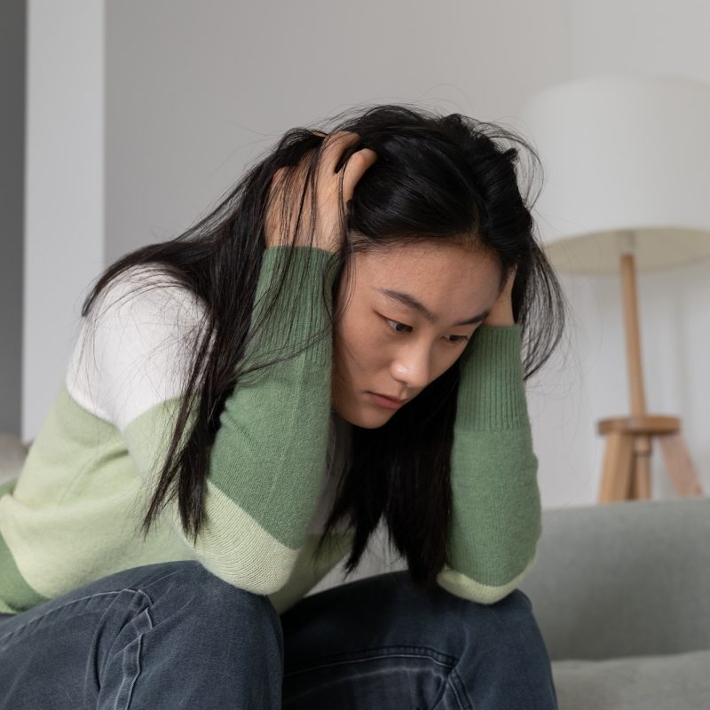 Anxious worried Asian millennial girl holding head in hands dealing with depression after abortion